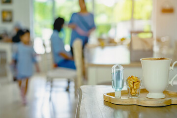 Mini portable alcohol gel bottle to kill Corona Virus(Covid-19) and biscuits and coffee cup on table with blurred image of a family eating at restaurant in background. Health care concept.
