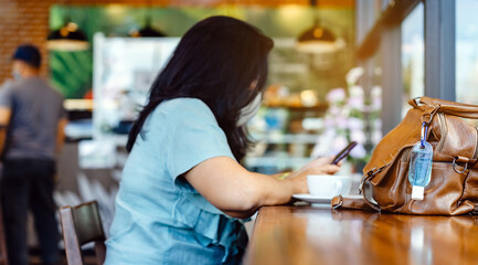 Mini alcohol gel bottle to kill Corona Virus(Covid-19) hang on a brown leather shoulder bag with hot coffee on table in cafe.New normal lifestyle.Health care concept.Selective focus on alcohol gel