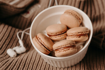 white headphones and caramel macaroons on a sweater. cozy autumn photography. photograph of food in brown tones. winter Playlist