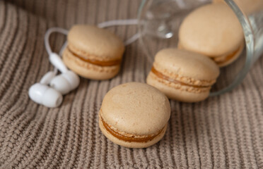 white headphones and caramel macaroons on a sweater. cozy autumn photography. photograph of food in brown tones. winter Playlist