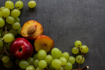 Beautiful fresh fruits on dark grey table: green grapes, nectarines, apricot. Summer fruits top view. 
