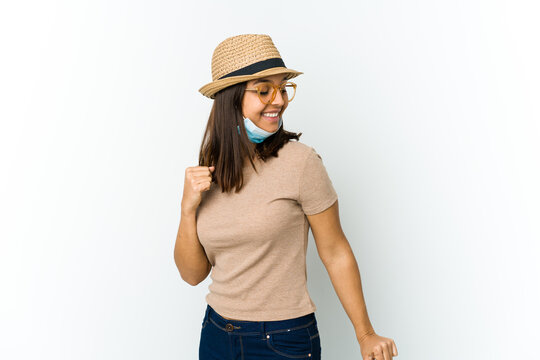 Young Latin Woman Wearing Hat And Mask To Protect From Covid Isolated On White Background Dancing And Having Fun.