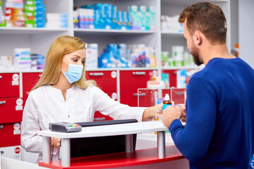 Obraz premium young professional druggist give medications to customer in modern drugstore, consult and recommend, wearing medical mask protecting from coronavirus covid-19