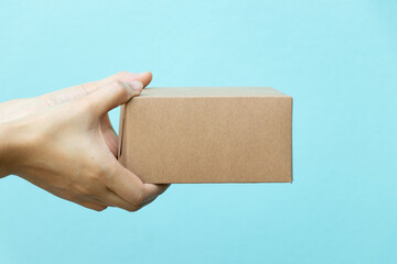 Woman hand hold the brown corrugated box on blue  wall background with copy space