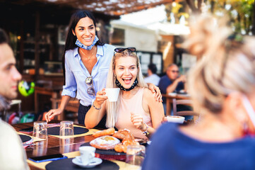 Group of happy friends having breakfast in the restaurant with face masks in the coronavirus time - New normal lifestyle concept with happy people having fun together outdoors.