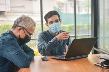 Fototapeta premium Asian man two people talking in office and working by computer notebook, Man face mask protect coronavirus covid 19