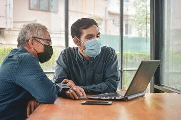 Asian man two people talking in office and working by computer notebook, Man face mask protect coronavirus covid 19