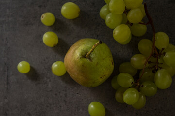 Still life with green pears and grapes on dark grey textured background. Summer fruits close up photo. 