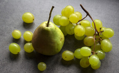 Still life with green pears and grapes on dark grey textured background. Summer fruits close up photo. 