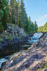 Plain waterfall Kivach.Long multistage flat waterfall. Seething waves and water falling on stones are visible. The slopes are rocky, spray and rainbow are visible. Russia, Karelia, Kivach
