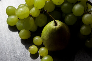 Still life with green pears and grapes on dark grey textured background. Summer fruits close up photo. 