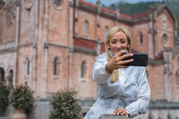 A young woman lowers her mask to take a Selfie in front of a monument in Spain. Covid Time.