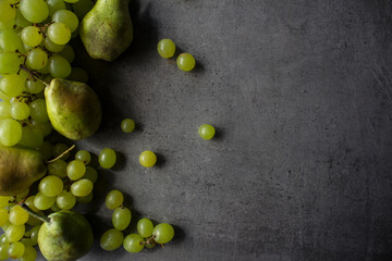 Green grapes and pears on dark grey textured background. Summer fruits border.  Beautiful top view photo with copy space. 