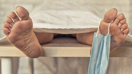 Close-up of dead men feet in a morgue with a medical mask on a toe. An unrecognizable woman has died from the coronavirus