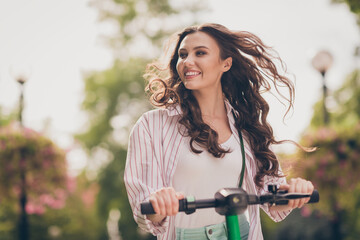 Photo of attractive young happy girl curly brown hair fun enjoy ride electric scooter outside