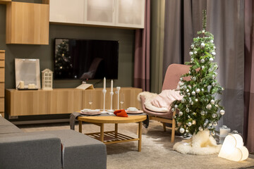 Cozy bright living room decorated with a Christmas tree with silver balls.