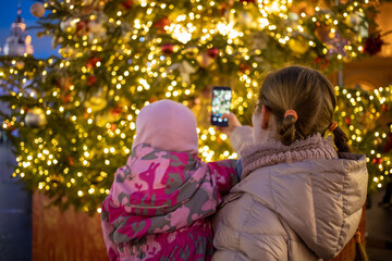 mom and baby in her arms photographing a Christmas tree at a street fair. back view