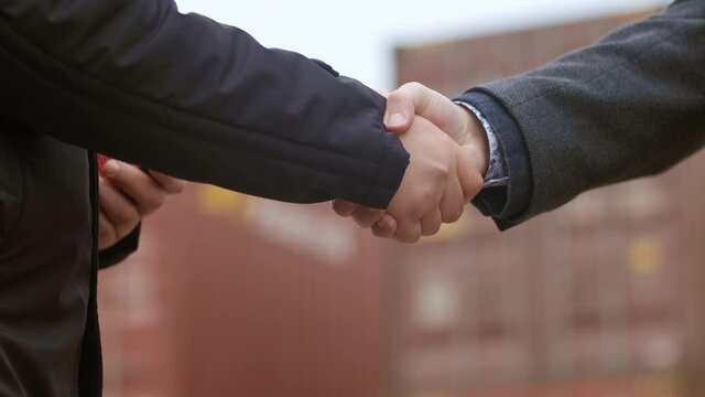 Businessmen Engineers shake hands as they load a container from a container yard onto a cargo ship for global import and export, supporting the concept of logistics. Close-up.