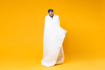 Full length of smiling young bearded man in pajamas home wear sleep mask standing wrapping in...