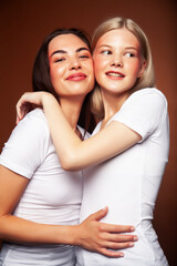 two pretty diverse girls happy posing together: blond and brunette on brown background, lifestyle people concept