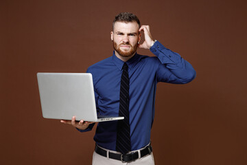 Preoccupied bearded young business man in blue shirt tie working on laptop pc computer put hand on head isolated on brown colour background studio portrait. Achievement career wealth business concept.