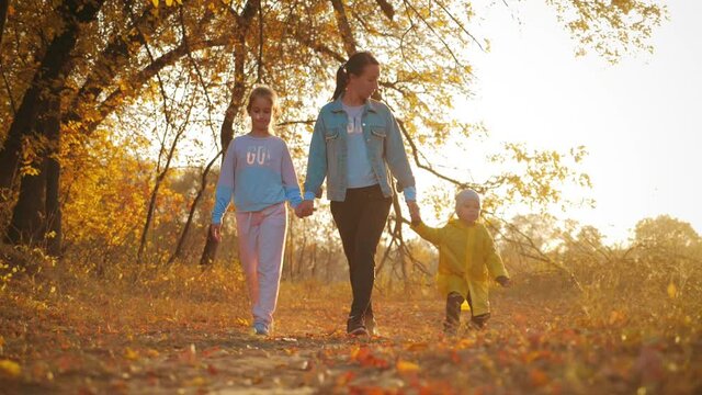 Mother and two children walking in the park and enjoying the beautiful autumn nature. Happy family on autumn walk.