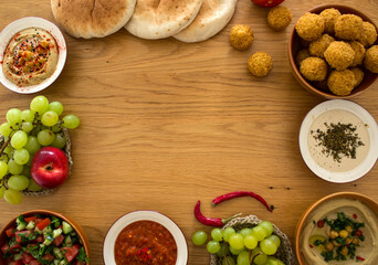 Food frame or border made of traditional Israeli meals: hummus, falafels, pita bread and different sauces on wooden table. Authentic dishes top view photo with copy space. 