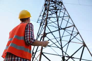 Electrical engineer with walkie talkie near high voltage tower, low angle view - Powered by Adobe