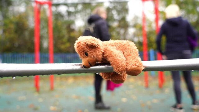 Lost Teddy bear lying on swing with rain drops in rainy day,Lonely or sad brown bear lied down alone with blurry kids and parent playing swing in the park background, International missing children's 