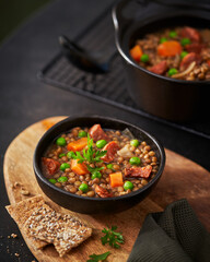 Traditional Spanish dish of lentil stew with chorizo and potatoes on a dark background, mediterranean food recipe. Selective focus.