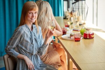 portrait of caucasian woman with glass of white wine in cafe or restaurant. young blonde woman sits posing, concept of celebration, enjoying alcohol, style and fashionable lifestyle