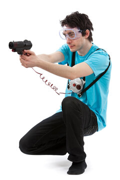 Studio photo of dark haired man with light blue t shirt and goggles using laser toy gun. Isolated on white background.