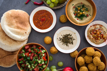 Traditional food of Israel on dark grey background with copy space. Colorful authentic meals top view photo: plate of hummus, falafels, salad, pita bread and tahini sauce. 