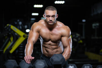 Fototapeta na wymiar Young adult bodybuilder is choosing a dumbbell for training weight lifting in gym