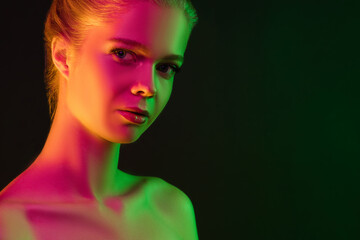 Inspired. Portrait of female fashion model in neon light on dark studio background. Beautiful caucasian woman with trendy make-up and well-kept skin. Vivid style, beauty concept. Close up. Copyspace