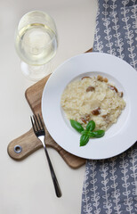 Vegetarian gourmet mushroom risotto on a white plate, yellow background, served with a glass of white wine. A northern Italian rice dish cooked with broth until it reaches a creamy consistency.