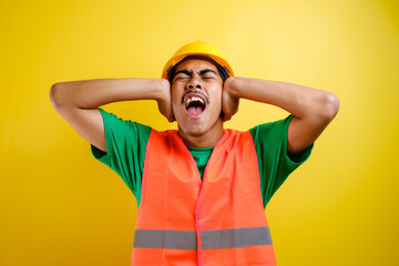 Worker wearing security helmet covering ears with fingers with annoyed expression