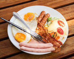 The English breakfast consists of fried eggs, bacon, sausage, and green salad.