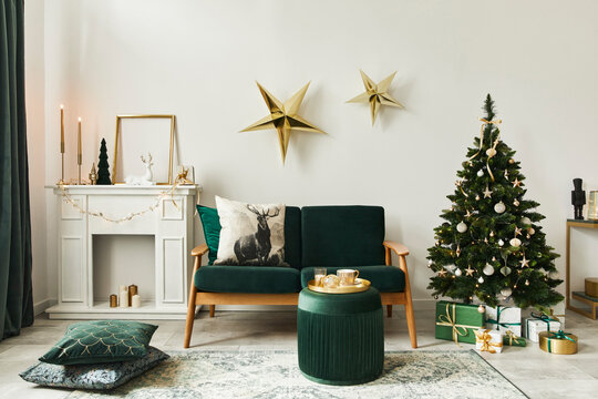 Stylish christmas living room interior with green sofa, white chimney, christmas tree and wreath, stars, gifts and decoration. Family time. Template.