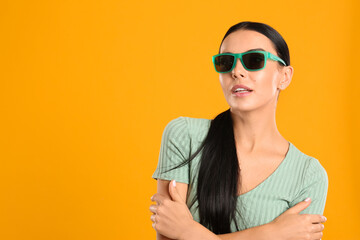 Beautiful woman wearing sunglasses on yellow background. Space for text