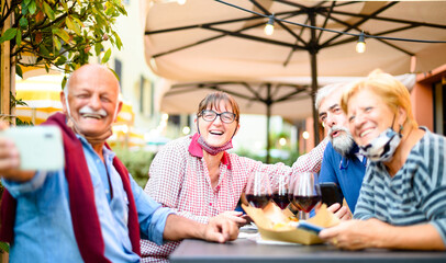 Senior couples taking selfie at restaurant bar with face masks - New normal lifestyle concept with happy people having fun together outdoors in covid-19 time - Focus on woman with glasses - Powered by Adobe