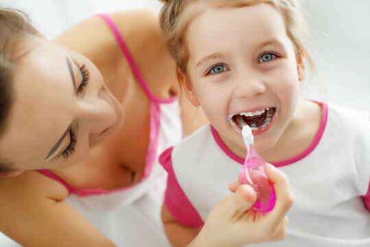 Mother and her daughter brush their teeth with toothbrushes in the bathroom at home. Mom and baby girl in home clothes. High quality photo.