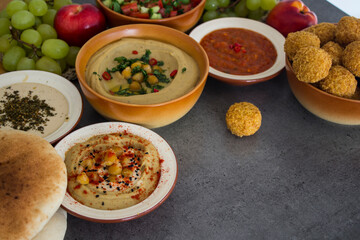 Traditional food of Israel on dark grey background with copy space. Colorful authentic meals top view photo: plate of hummus, falafels, salad, pita bread and tahini sauce. 