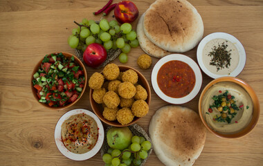   Authentic food of Middle East. Plate of hummus, falafels, pita bread, harissa sauce, tahini, fresh salad and fruits on wooden table. Traditional meals of Israel top view photo. Beautiful food pictur