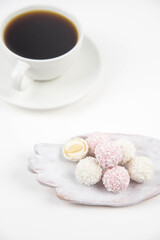 White coconut candy balls on handmade plate. Coconut cookies on white background with the cup of tea. Teapot with black tea. 