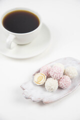 White coconut candy balls on handmade plate. Coconut cookies on white background with the cup of tea. Teapot with black tea. 