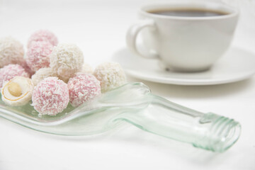 White coconut candy balls on handmade upcycle plate from the bottle. Coconut cookies on white background with the cup of tea. Teapot with black tea. 