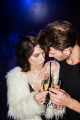 Man and seductive woman toasting with glasses of champagne, while looking at each other with backlit on black