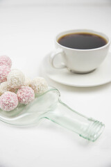 White coconut candy balls on handmade upcycle plate from the bottle. Coconut cookies on white background with the cup of tea. Teapot with black tea. 