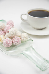 White coconut candy balls on handmade upcycle plate from the bottle. Coconut cookies on white background with the cup of tea. Teapot with black tea. 